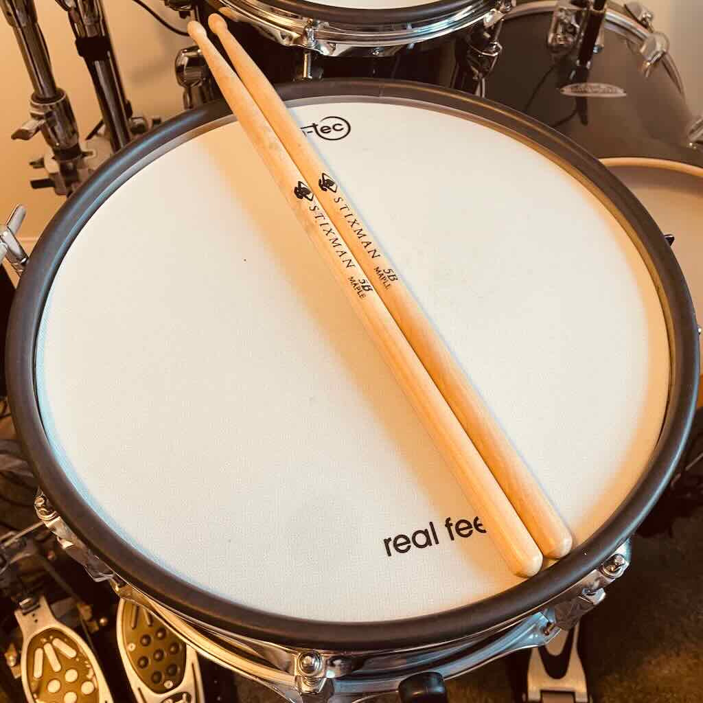A pair of stickman 5B maple drumsticks resting on an electronic drum pad